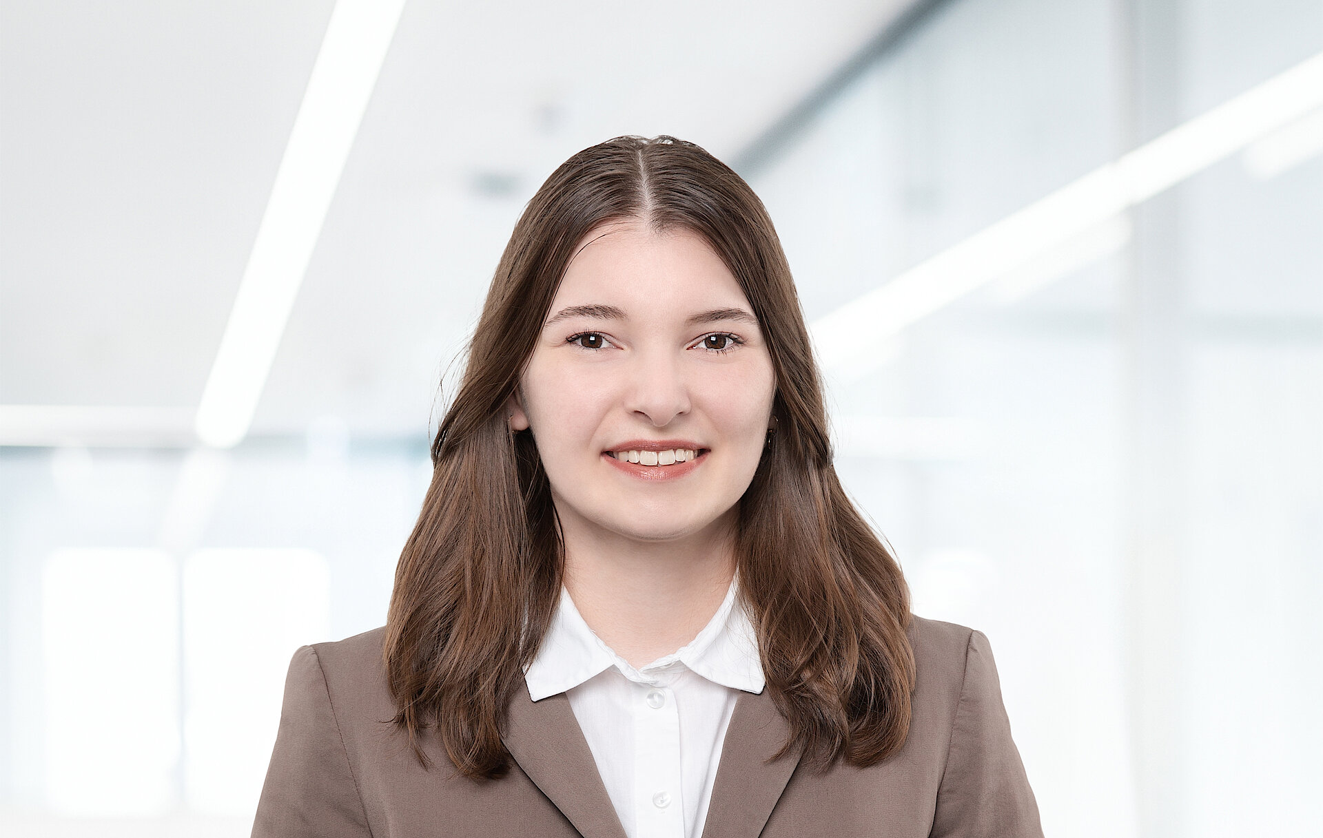 Porträt einer Frau in einem Business-Anzug, die in einer Büroumgebung lächelt.