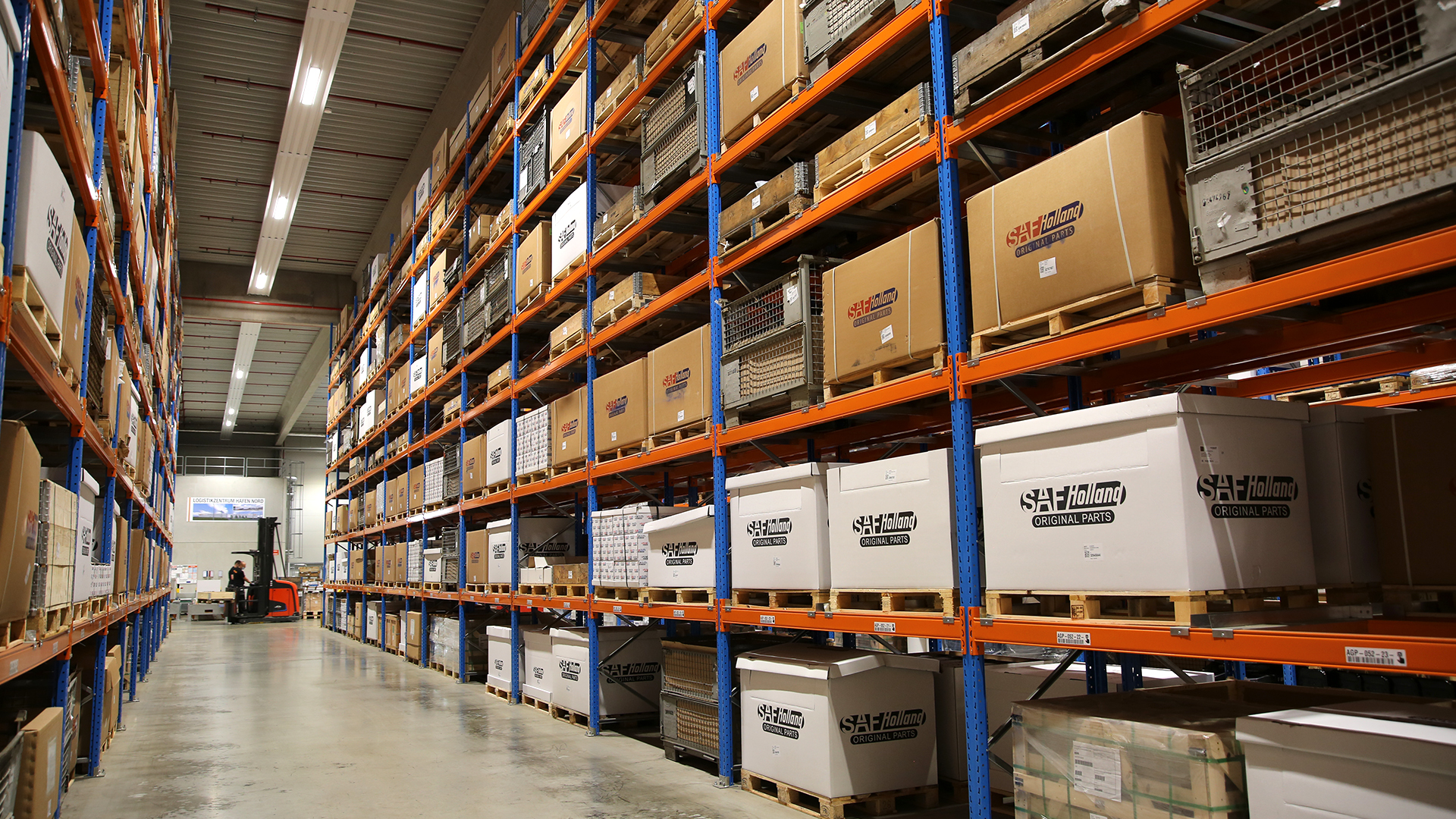 Warehouse aisle with stacked SAF-HOLLAND parts, showcasing organized shelving and logistics efficiency.