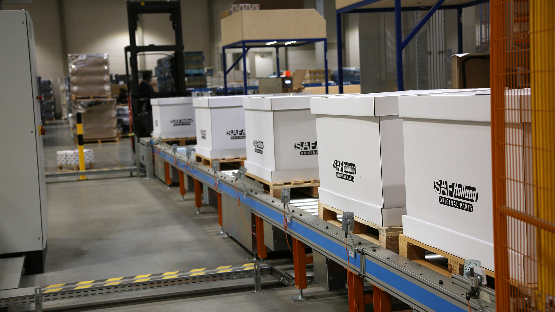 Boxes labeled "SAF-HOLLAND Original Parts" on a conveyor in a warehouse.