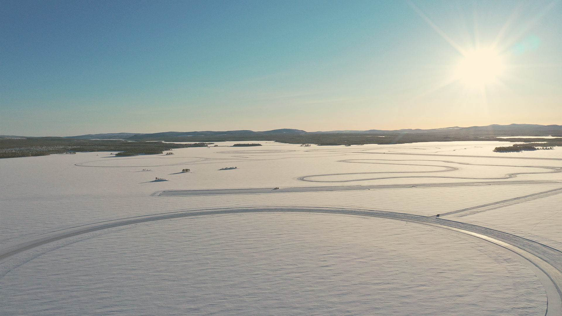 Aerial view of a snow-covered landscape with curving test tracks under the sun.