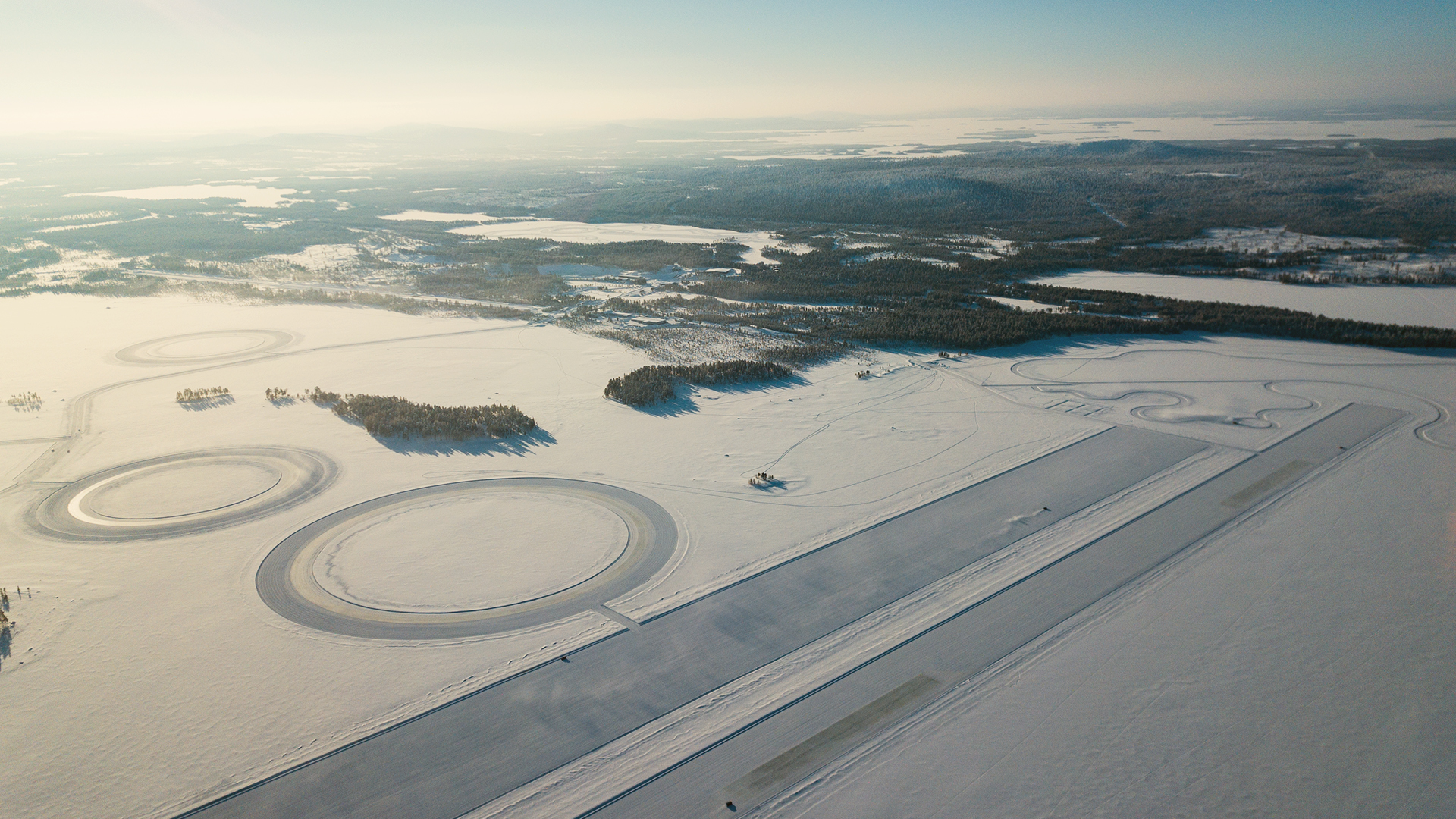 Aerial view of a snow-covered test track facility with circular and linear tracks.