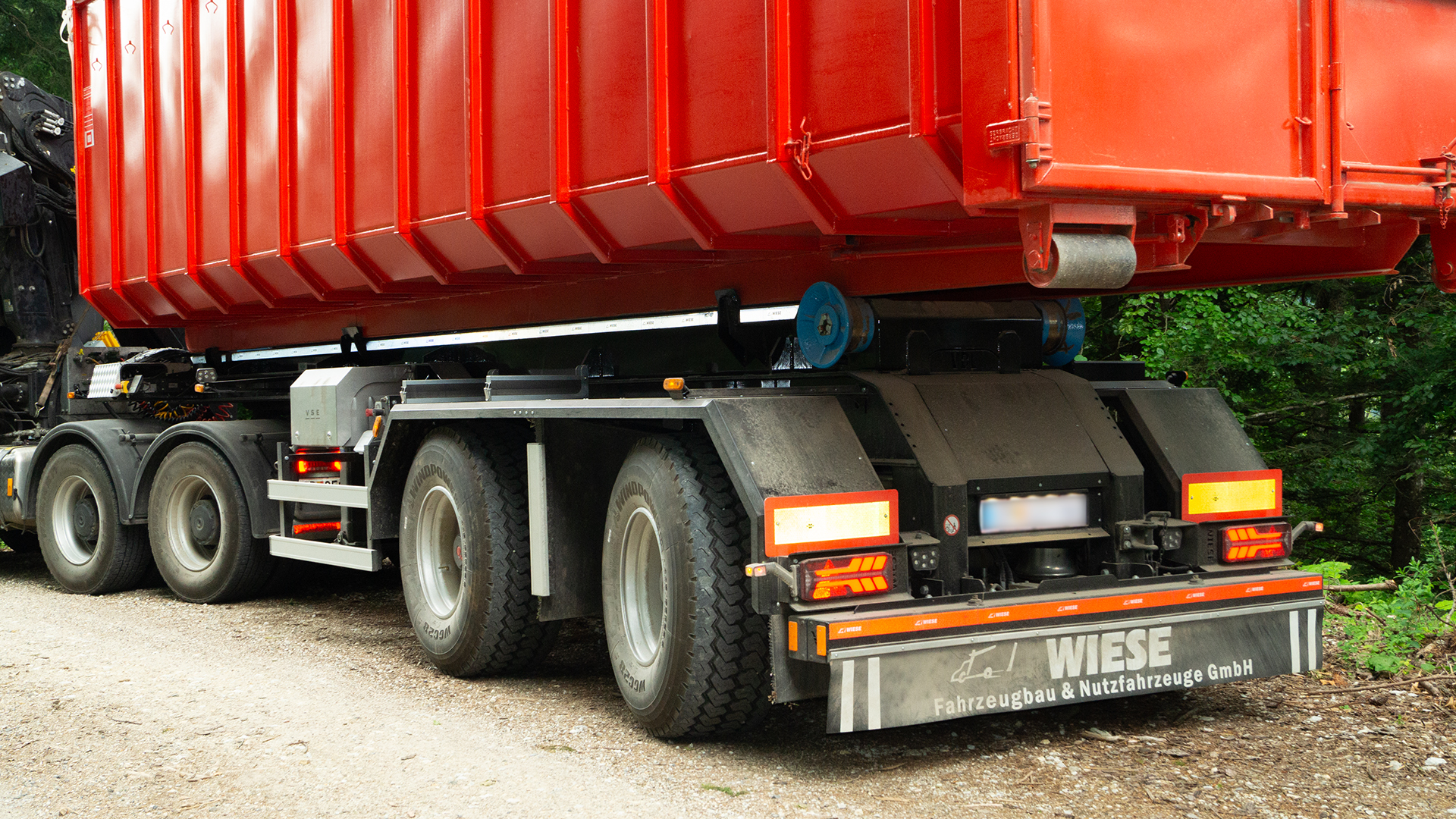 Truck with a red container using SAF-HOLLAND suspension system parked on a dirt road.